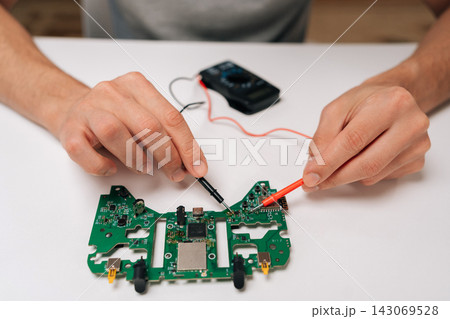 Repairman hands troubleshooting game controller circuit board with multimeter, checking electronic components and diagnosing potential issues during the repair and maintenance process. Repairman hands troubleshooting game controller circuit board with multimeter, checking electronic components and diagnosing potential issues during the repair and maintenance process. 143069528