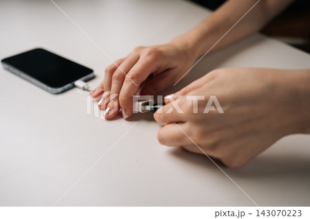 Close-up hands of unrecognizable woman connecting USB flash drive to smartphone through adapter cable, facilitating data transfer and expanding mobile storage sitting on white table, closeup. 143070223