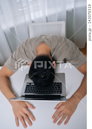 Vertical top view of exhausted freelancer male feeling burnout and stress, laying sleeping with face on laptop after working long hours, experiencing fatigue and overwork in workplace or home office. 143070319