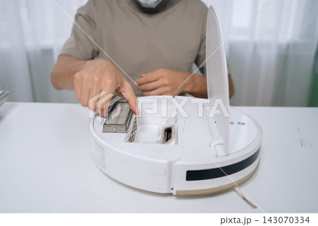 Person performing routine maintenance on robot vacuum cleaner, removing dirty filter to ensure efficient floor cleaning and smart home appliance longevity, close-up cropped shot. 143070334