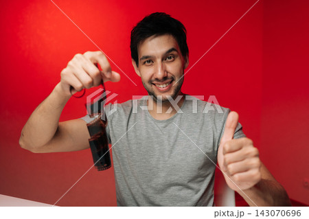 Portrait of enthusiastic young man smiling at camera. Concept of strip of film negative giving thumbs up gesture, celebrating art of traditional photography on vibrant red background. 143070696
