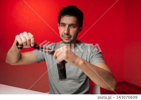 Smiling young creative man in grey shirt examines analog film negative. Studio portrait with direct lighting on vibrant red background. Concept of photography, hobby, nostalgia, creative process. 143070699