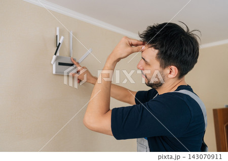 Stressed technician has problems installing Wi-Fi router. Confused man looking frustrated trying to set up internet connection at home. Concept for technology issues, network failure, DIY repair. 143070911