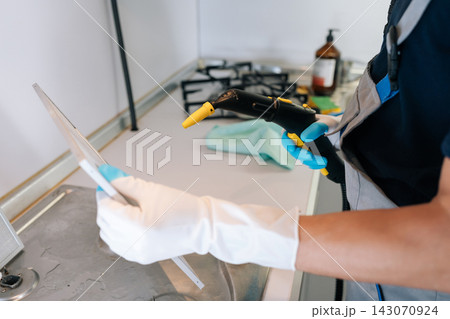 Professional cleaner in uniform and gloves steaming and sanitizing greasy kitchen range hood filter during deep clean service, removing grime for spotless, chemical free results. 143070924