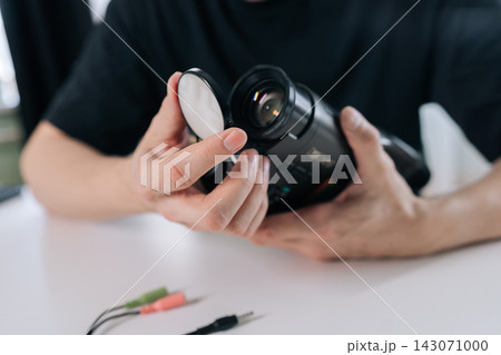 Hands removing lens cap from old camcorder on white table, close-up of vintage video camera being prepared for recording, nostalgia and analog videography tools. 143071000