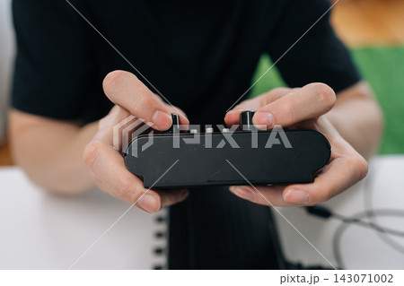 Person hands manipulating knobs and buttons on black audio electronics device, fine tuning settings for sound or music production in close-up view. 143071002