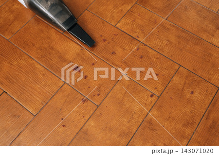 Portable vacuum cleaner working on wooden parquet floor. Effectively cleaning crumbs and small debris. Illustrating a convenient method for quick tidying and maintaining order in a domestic setting. Portable vacuum cleaner working on wooden parquet floor. Effectively cleaning crumbs and small debris. Illustrating a convenient method for quick tidying and maintaining order in a domestic setting. 143071020