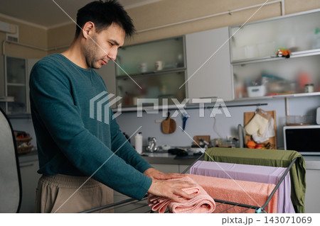 Side view of man performing daily household chores, hanging freshly washed towels on drying rack in kitchen setting, demonstrating domestic responsibility. Concept of household chores and housework. Side view of man performing daily household chores, hanging freshly washed towels on drying rack in kitchen setting, demonstrating domestic responsibility. Concept of household chores and housework. 143071069
