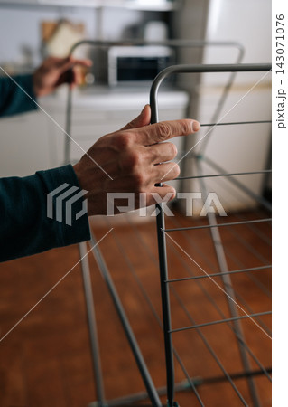 Vertical shot of male hands opening indoor clothes drying rack, performing domestic chores and preparing for daily laundry routine at home. Concept of housekeeping and cleaning. Vertical shot of male hands opening indoor clothes drying rack, performing domestic chores and preparing for daily laundry routine at home. Concept of housekeeping and cleaning. 143071076