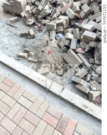 Road repair site with scattered bricks and uneven surface near paved walkway in urban area Road repair site with scattered bricks and uneven surface near paved walkway in urban area 143071153