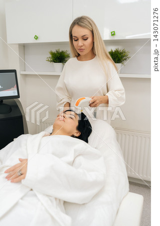 Skilled female cosmetologist using professional laser machine for photorejuvenation and skin resurfacing treatment on woman face in specialized dermatology clinic. 143071276