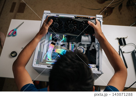 High-angle view of computer technician carefully inserting high-performance graphic card inside gaming desktop, upgrading powerful system with vibrant RGB lighting for maximum computing potential 143071288