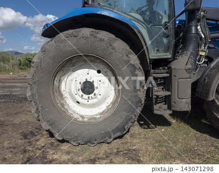 Close up of a modern blue farm tractor showing cabin and large muddy wheel 143071298