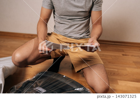 Close-up cropped shot of man following written instructions to assemble new flat-pack furniture, focusing on steps to build office chair on te hardwood floor, common home improvement and diy task. Close-up cropped shot of man following written instructions to assemble new flat-pack furniture, focusing on steps to build office chair on te hardwood floor, common home improvement and diy task. 143071325