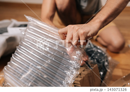 Close-up cropped shot of man unpacking office chair base wrapped in protective foam, hands preparing parts for assembly in home office diy furniture project, focused on setup and comfort. Close-up cropped shot of man unpacking office chair base wrapped in protective foam, hands preparing parts for assembly in home office diy furniture project, focused on setup and comfort. 143071326