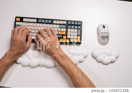 Top view of male hands typing on mechanical keyboard with custom keycaps and ergonomic cloud-shaped wrist rests, ensuring comfortable wrist support for extended computer work and productivity. Top view of male hands typing on mechanical keyboard with custom keycaps and ergonomic cloud-shaped wrist rests, ensuring comfortable wrist support for extended computer work and productivity. 143071388