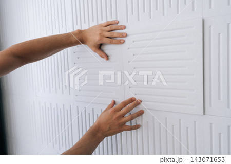 Hands installing soundproofing acoustic panels on a white studio wall, creating a quiet environment for sound dampening and noise reduction in a recording space. Hands installing soundproofing acoustic panels on a white studio wall, creating a quiet environment for sound dampening and noise reduction in a recording space. 143071653