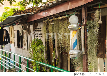 Colorful Barber Pole and Hanging Air Plants Beside Rustic Bangkok Storefront Colorful Barber Pole and Hanging Air Plants Beside Rustic Bangkok Storefront 143071694