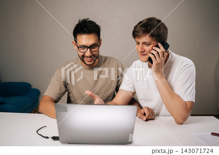 Portrait of successful young men brainstorming startup ideas, collaborating ona new business project, using laptop and smartphone for communication and strategy in modern home office. Portrait of successful young men brainstorming startup ideas, collaborating ona new business project, using laptop and smartphone for communication and strategy in modern home office. 143071724