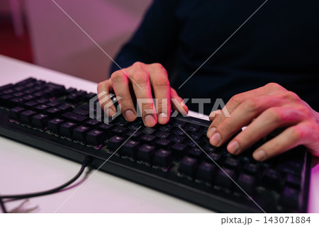 Close-up of male hands typing on black computer keyboard. Moody scene with pink neon lighting. Concept of programming, coding, hacking, cybersecurity, late night gaming. Close-up of male hands typing on black computer keyboard. Moody scene with pink neon lighting. Concept of programming, coding, hacking, cybersecurity, late night gaming. 143071884