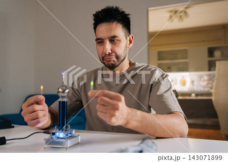 Surprised young man demonstrating tesla coil wireless power transmission, illuminating two light bulbs without direct contact, showcasing electricity, science and hobby experiment. 143071899