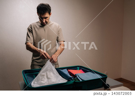 Portrait of traveler young man organizing baggage, packing shoes into a protective bag inside a luggage, preparing for an exciting journey, departure, or vacation. Portrait of traveler young man organizing baggage, packing shoes into a protective bag inside a luggage, preparing for an exciting journey, departure, or vacation. 143072003