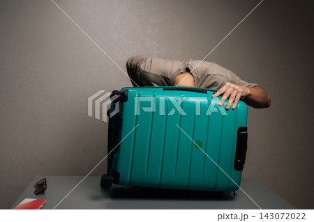 Man struggling to pack a vibrant teal suitcase for travel, organizing belongings, preparing for journey, experiencing challenges with baggage capacity. 143072022
