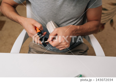 Close-up of electrician hands holding cable crimping tool, preparing white electrical wire for secure connection, performing precise task of installation or repair and ensuring proper conductivity. 143072034