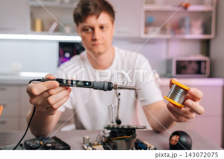 Man holding modern soldering iron and spool of solder wire, preparing to repair or assemble an electronic circuit board, concept of process of technical maintenance and diy electronics. 143072075
