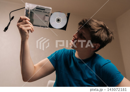 Man holding external optical disc drive with tray extended, showcasing modern peripheral hardware for data storage and multimedia playback on a laptop. Man holding external optical disc drive with tray extended, showcasing modern peripheral hardware for data storage and multimedia playback on a laptop. 143072181