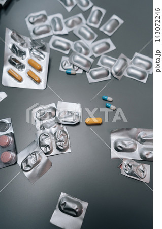 Vertical cropped shot of pills, capsules, empty blister packs scattered on gray surface, concepts of daily medication, healthcare reliance, pharmaceutical treatment, and medical therapy management. Vertical cropped shot of pills, capsules, empty blister packs scattered on gray surface, concepts of daily medication, healthcare reliance, pharmaceutical treatment, and medical therapy management. 143072246