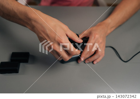 Top view of person placing red lithium-ion battery into dual-slot digital camera charger on gray table, actively powering up essential photography gear for creative work. 143072342