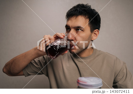 Close-up portrait of young man enjoying refreshing homemade berry compote from large glass jar, quenching thirst with natural drink, emphasizing healthy hydration and domestic canning. Close-up portrait of young man enjoying refreshing homemade berry compote from large glass jar, quenching thirst with natural drink, emphasizing healthy hydration and domestic canning. 143072411