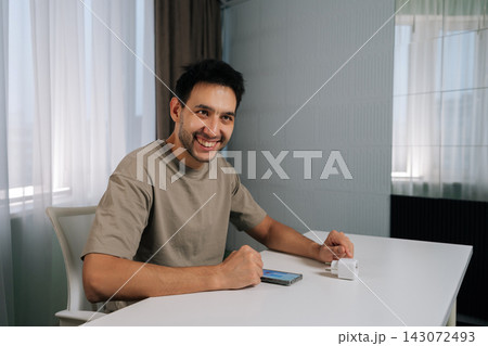 Cheerful young man holding smart socket and smartphone, smiling looking away, connecting smart home device for wireless automation, setup and iot control in modern apartment. Cheerful young man holding smart socket and smartphone, smiling looking away, connecting smart home device for wireless automation, setup and iot control in modern apartment. 143072493