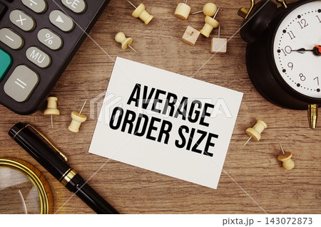 Average Order Size text written on notepad with pen, alarm clock, magnifying glass and calculator on wooden background 143072873
