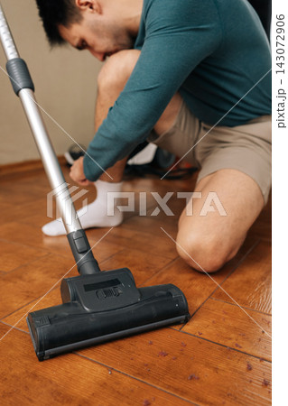 Two people sharing household chores, one holding using cordless vacuum cleaner while another getting dressed white sock, cleaning wooden floor. Concept of cleanliness and housekeeping. 143072906