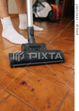 Vertical cropped shot of person cleaning wooden floor with vacuum cleaner, effectively removing scattered dirt and debris. Concept of household chores, cleanliness, residential maintenance activities. 143072907