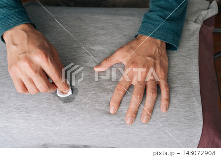 Top view of person hands cleaning wiping spill on gray fabric shirt using small white cloth soaked in cleaning agent, demonstrating household hygiene and laundry stain removal techniques. Top view of person hands cleaning wiping spill on gray fabric shirt using small white cloth soaked in cleaning agent, demonstrating household hygiene and laundry stain removal techniques. 143072908