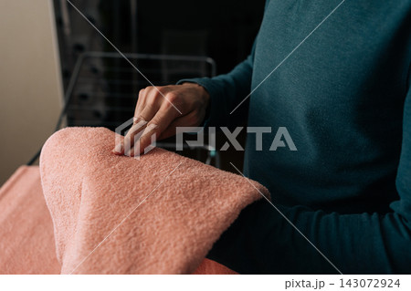 Close-up person hand checking texture and softness of freshly laundered pink towel, hanging on indoor clothes drying rack, representing daily domestic tasks and fabric care. 143072924