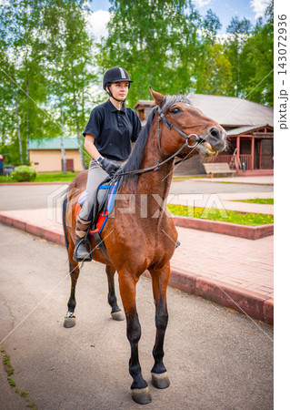 Lovely young woman wearing helmet riding her brown horse 143072936