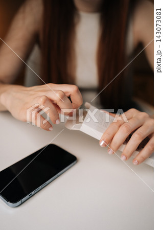 Close-up of female hands with manicured nails carefully opening white retail package containing new phone adapter cable, ready to connect and charge. Concept of smartphone unboxing process. 143073081
