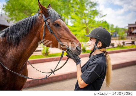 Lovely young woman wearing helmet stroking to her brown horse 143073086