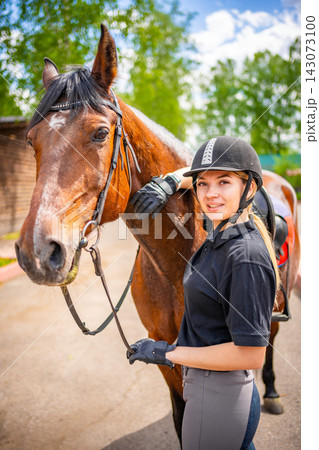 Lovely young woman wearing helmet stroking to her brown horse Lovely young woman wearing helmet stroking to her brown horse 143073100