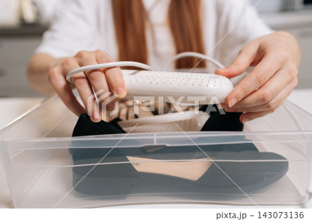 Closeup cropped shot of female placing electric shoe dryer into black suede footwear inside clear plastic container, focusing on home care and maintenance for drying shoes and sandals effectively. Closeup cropped shot of female placing electric shoe dryer into black suede footwear inside clear plastic container, focusing on home care and maintenance for drying shoes and sandals effectively. 143073136