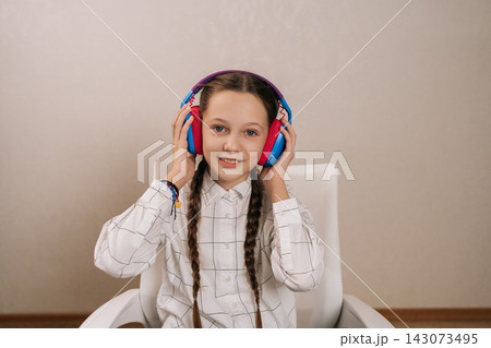 Young girl with pigtails holding colorful headphones on ears, happily engaging with audio entertainment, representing childhood leisure, learning, and digital enjoyment. 143073495