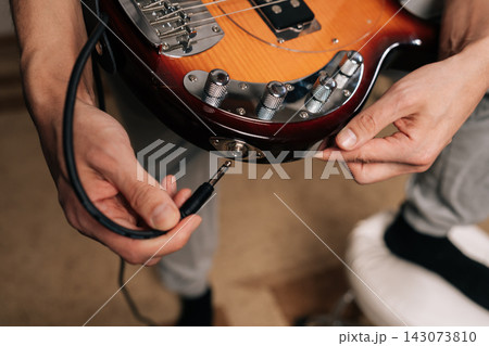 Top view cropped shot of musician connecting instrument cable to electric bass guitar, plugging in audio jack, preparing for practice, recording session, or live performance, focusing on music tools. 143073810