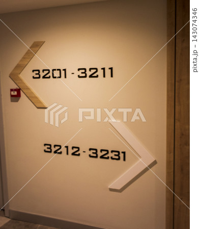Modern hotel corridor wall signage with wooden arrows indicating room number directions. Indoors Modern hotel corridor wall signage with wooden arrows indicating room number directions. Indoors 143074346