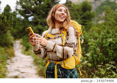 A person stands on a rocky trail in a forest. They look at their phone while wearing a backpack. A person stands on a rocky trail in a forest. They look at their phone while wearing a backpack. 143074466