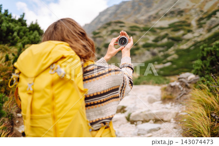 Person with backpack stands on rocky path in mountainous area while taking picture of waterfall. 143074473