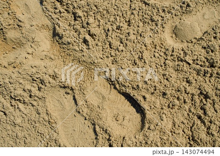 top-down close-up shot of a patch of damp yellow sand with a light human footprint compression 143074494